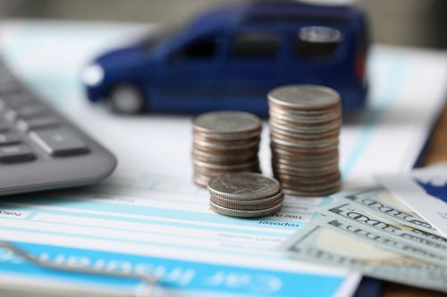 Close-up of important papers about car insurance, money and pile of coins. Blue toy machine on folder on background