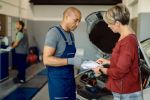 Black auto mechanic and his customer going through paperwork in a repair shop.